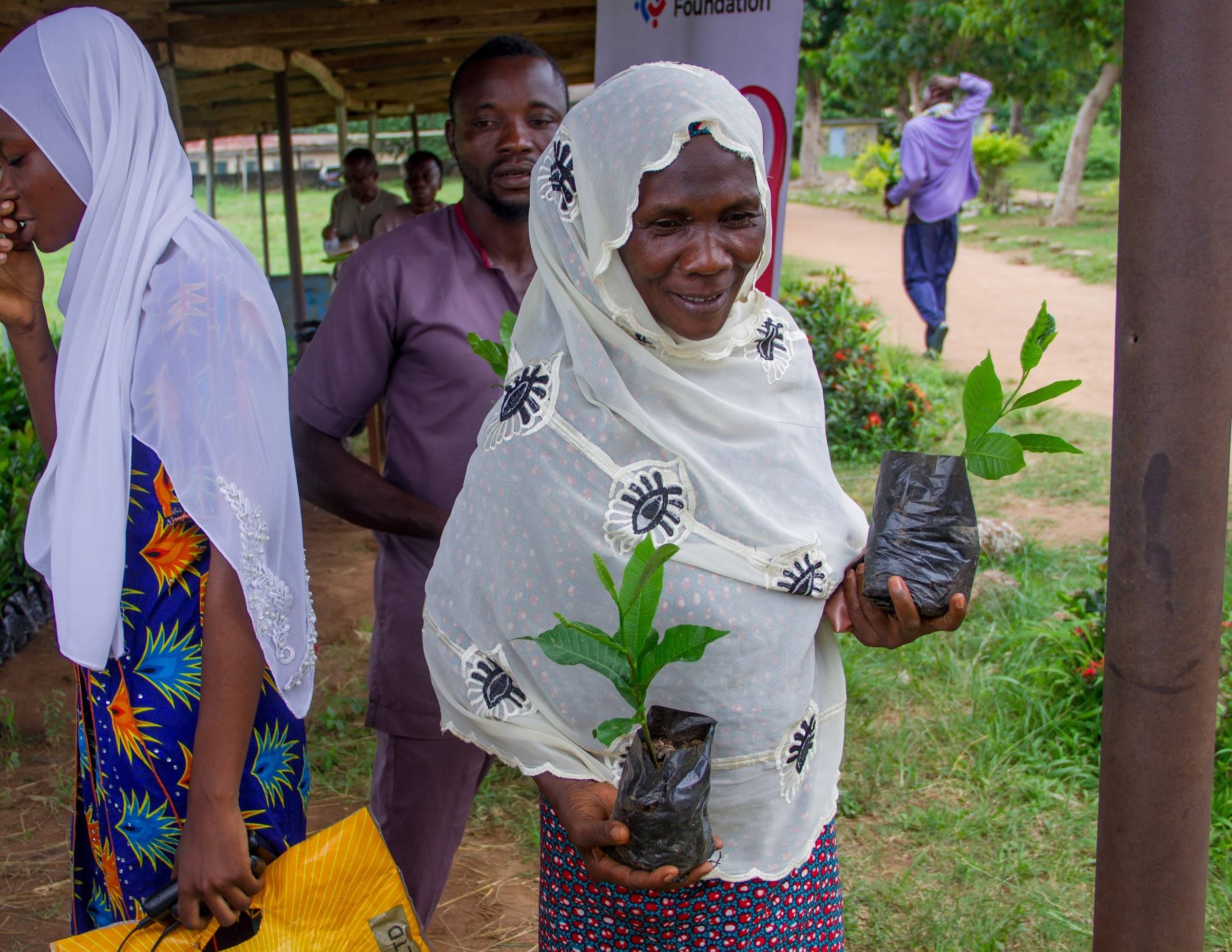A woman holding a young cashew seedling in a nursery bag at a JIFE Foundation distribution.